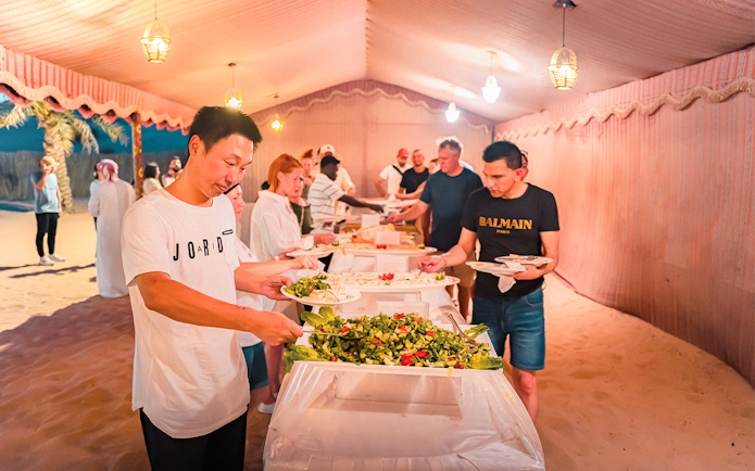Guests serving themselves at a buffet during Abu Dhabi evening desert safari with BBQ dinner.