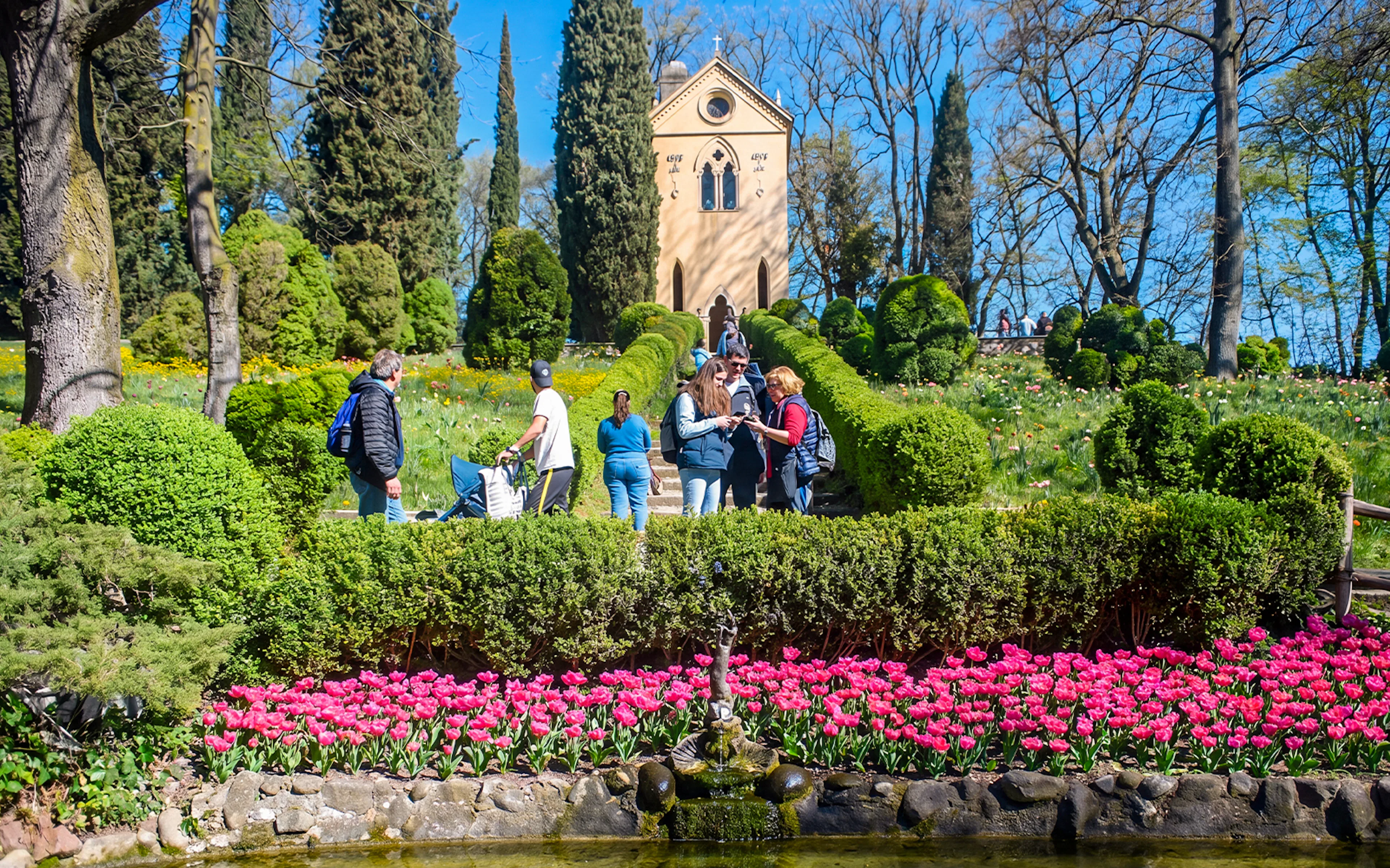 Tourists exploring Hermitage of Laura at Parco Giardino Sigurtà with vibrant gardens.