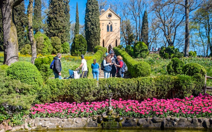 Tourists exploring Hermitage of Laura at Parco Giardino Sigurtà with vibrant gardens.