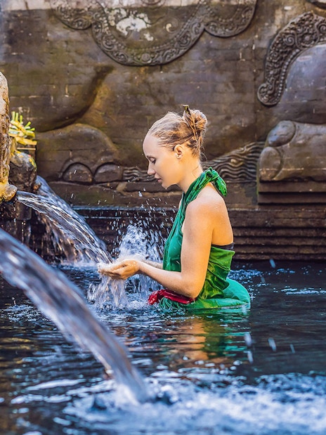 Woman at Tirta Empul Temple's holy spring during Kintamani sunrise tour.