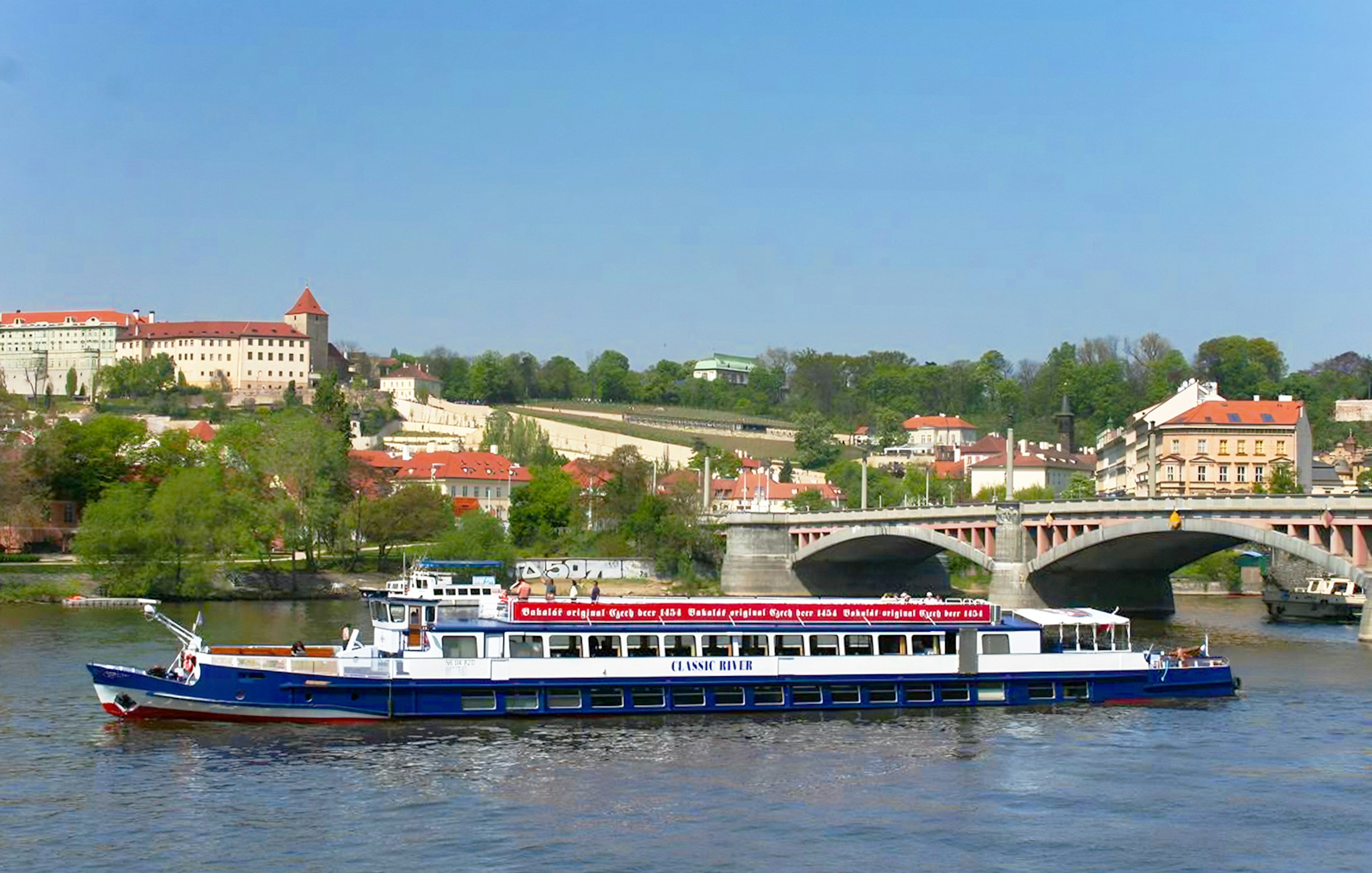 River cruise boat on Vltava River with Prague Castle in the background.