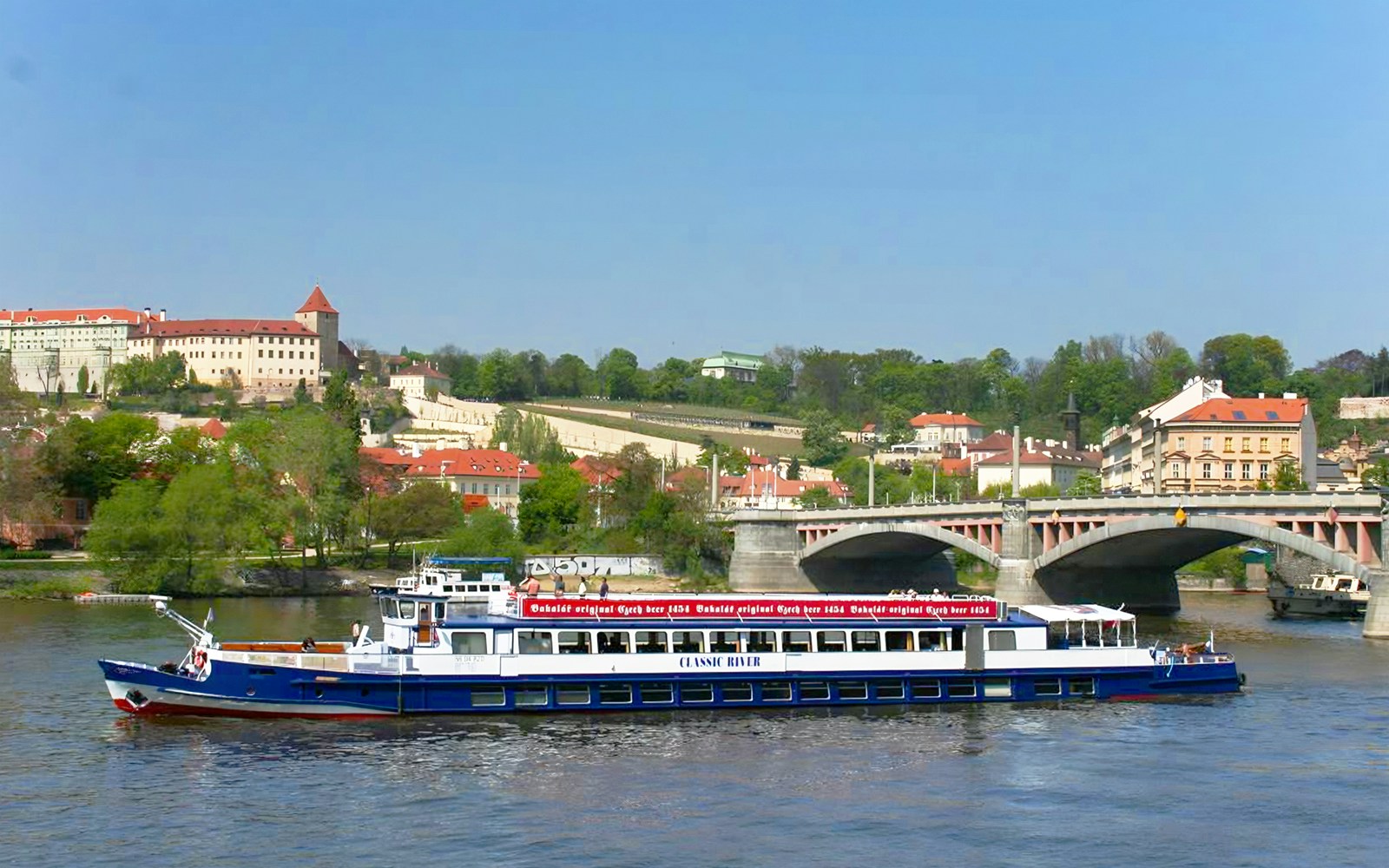 River cruise boat on Vltava River with Prague Castle in the background.