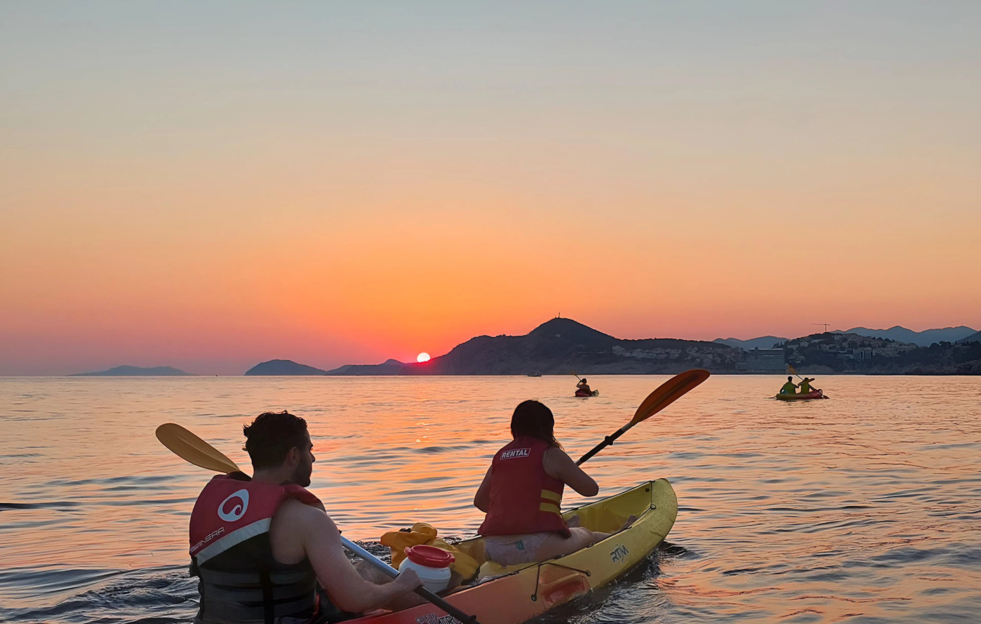 Kayakers paddling at sunset near coastal mountains.