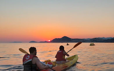 Kayakers paddling at sunset near coastal mountains.
