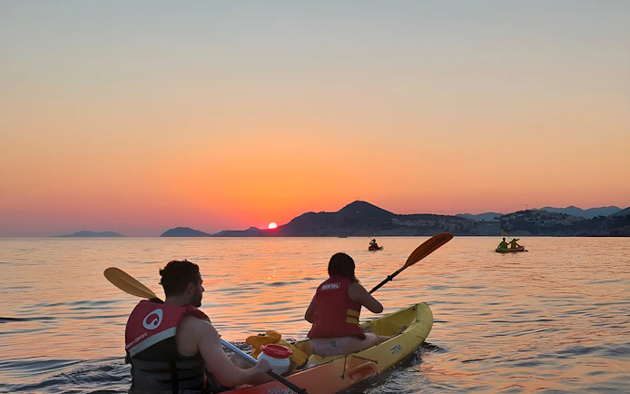 Kayakers paddling at sunset near coastal mountains.
