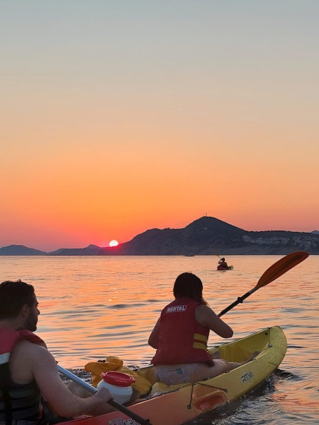 Kayakers paddling at sunset near coastal mountains.