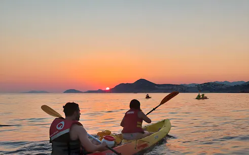 Kayakers paddling at sunset near coastal mountains.