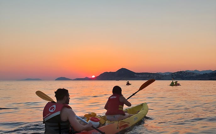 Kayakers paddling at sunset near coastal mountains.