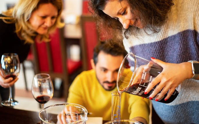 Wine blending workshop participants pouring wine into a beaker at a winery.