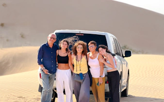 Group posing by SUV in Abu Dhabi desert during evening safari tour.