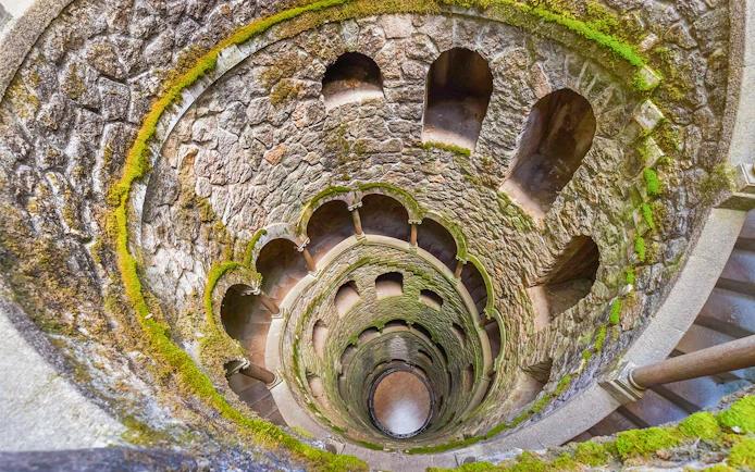 Quinta da Regaleira Initiation Well in Sintra, Portugal, with moss-covered stone walls.