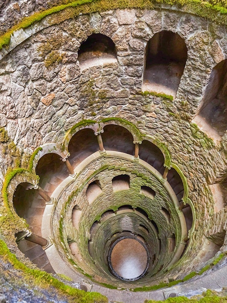 Quinta da Regaleira Initiation Well in Sintra, Portugal, with moss-covered stone walls.