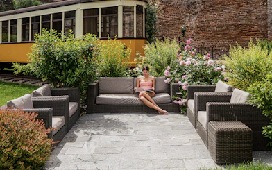 Outdoor seating area at QC Terme Milano with a woman reading, surrounded by greenery and flowers.