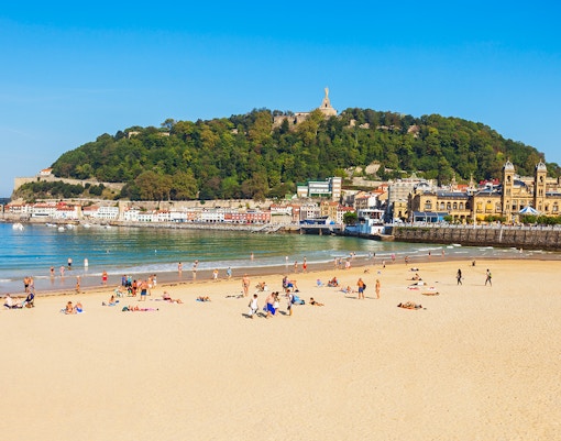 Strandbesucher am Strand La Concha mit dem Monte Urgull in San Sebastián, Spanien.
