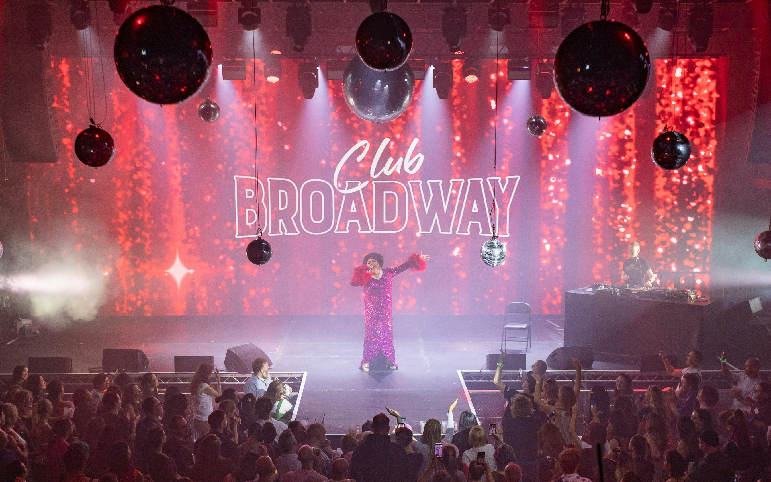 Performer on stage at Club Broadway show, West End, with audience and DJ.