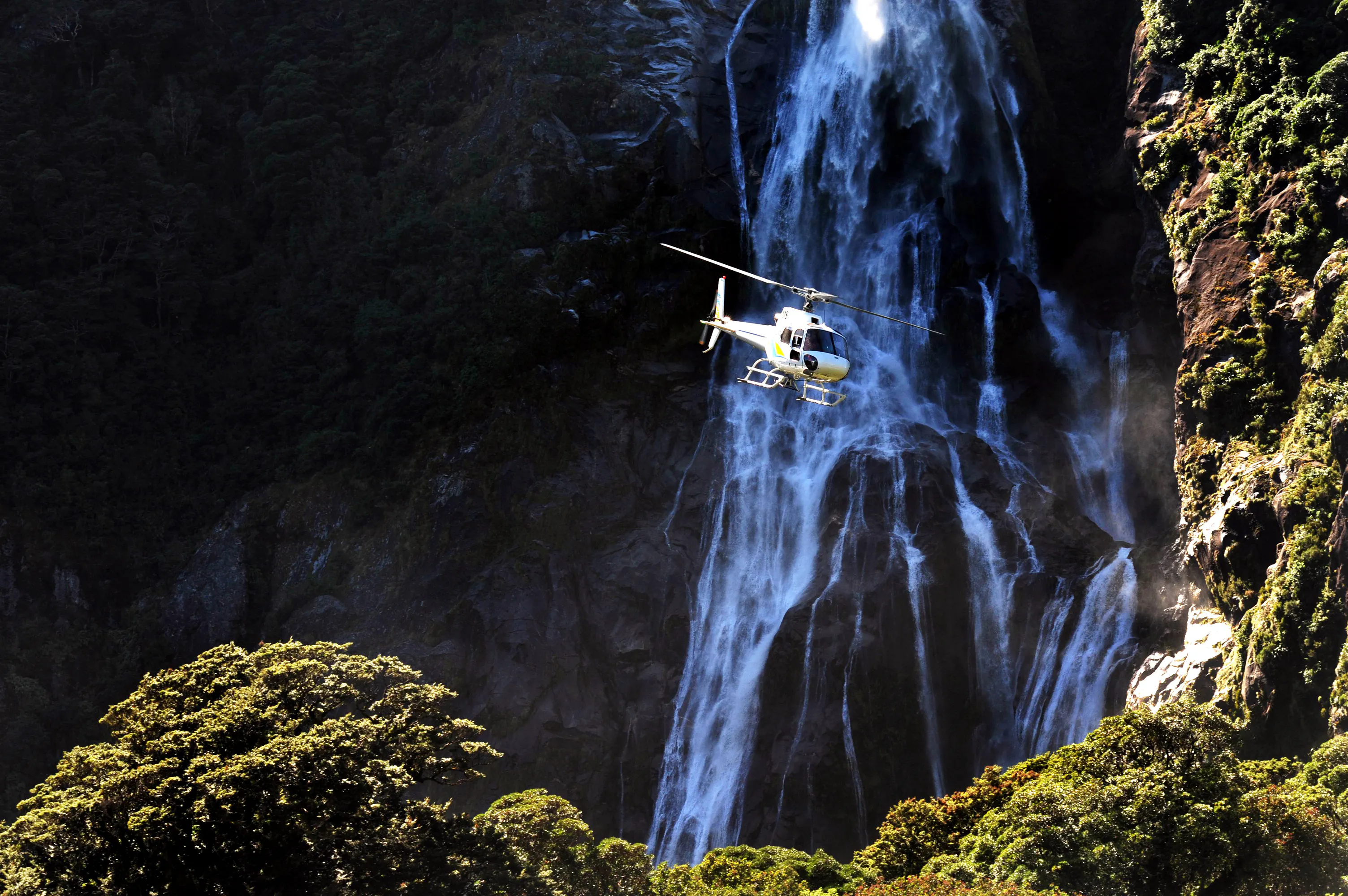 Helicopter flying near waterfall in Milford Sound, New Zealand Fiordland.