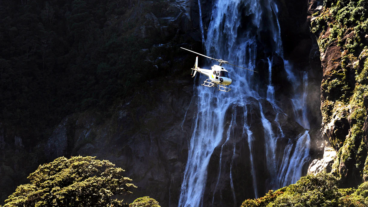 Helicopter flying near waterfall in Milford Sound, New Zealand Fiordland.