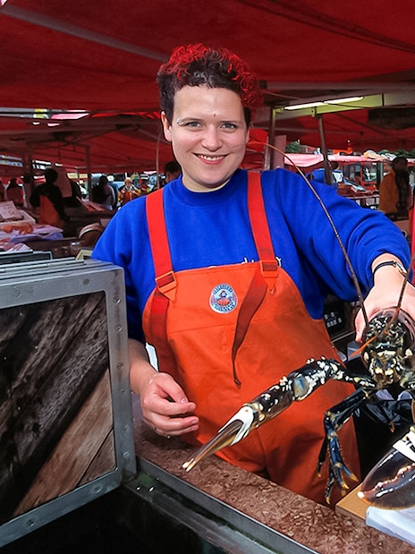 Bergen fish market vendor holding lobster, showcasing seafood selection.