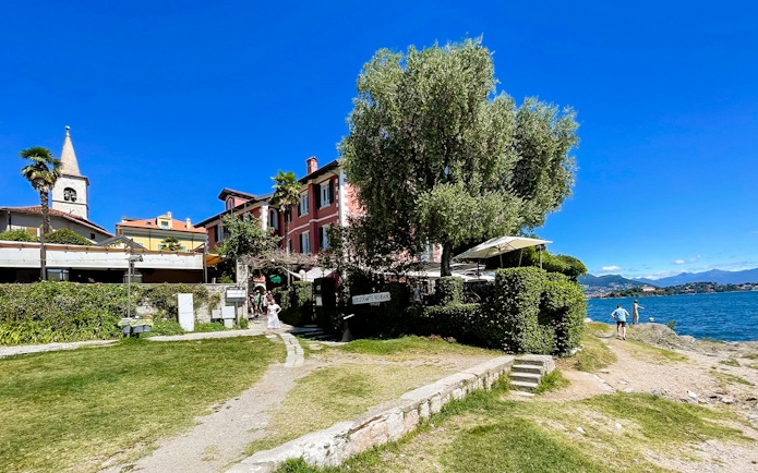 Lakeside view of a colorful building and church tower on Isole Borromee, Italy, with tourists walking nearby.