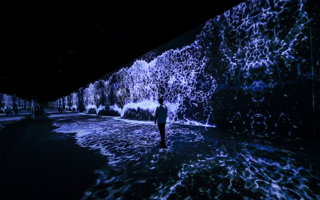 Person walking through ARTE Museum Dubai's Starry Beach exhibit with digital waves.