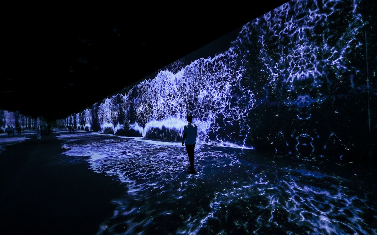 Person walking through ARTE Museum Dubai's Starry Beach exhibit with digital waves.