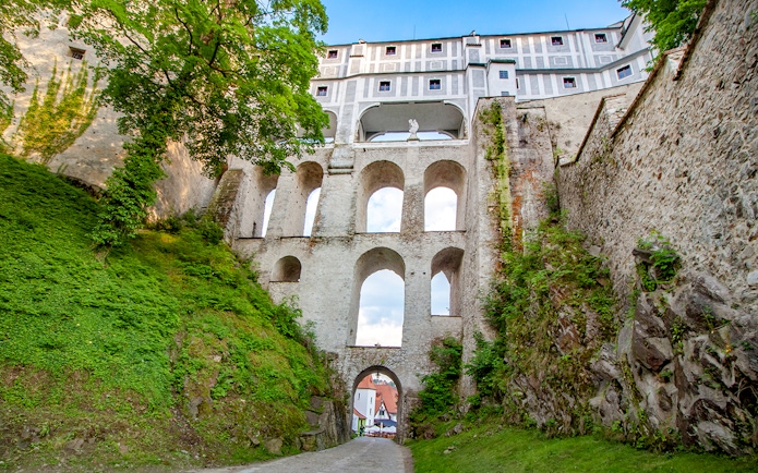 Bridge over Cesky Krumlov castle with stone arches and greenery.