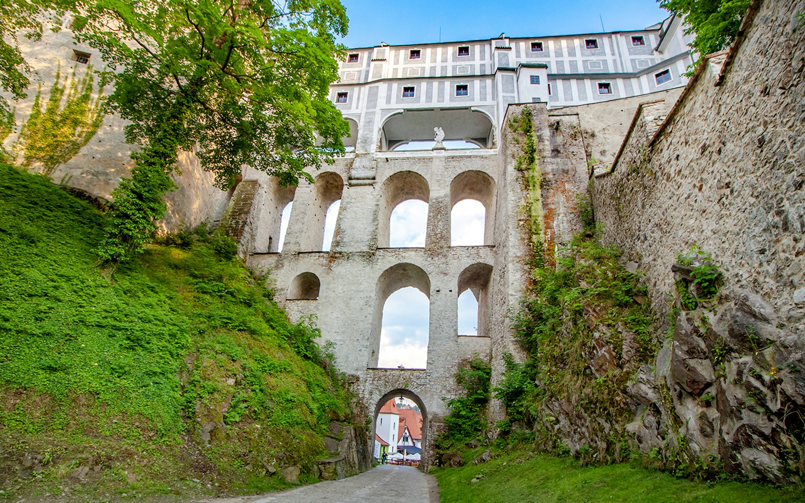 Bridge over Cesky Krumlov castle with stone arches and greenery.