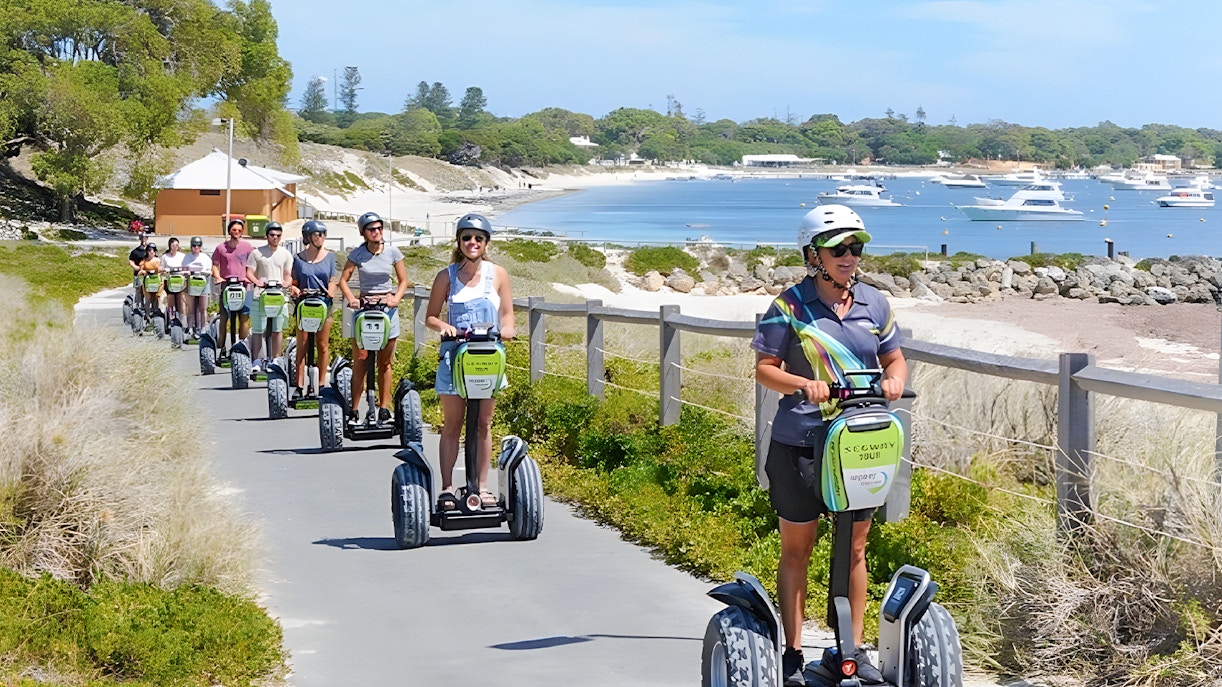 Tourists on Segways exploring Rottnest Island with ferry in background, departing from Perth or Fremantle.