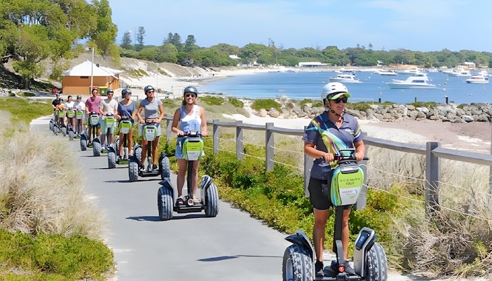 Tourists on Segways exploring Rottnest Island with ferry in background, departing from Perth or Fremantle.