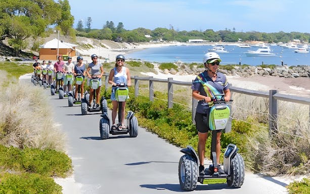 Tourists on Segways exploring Rottnest Island with a ferry visible in the background.