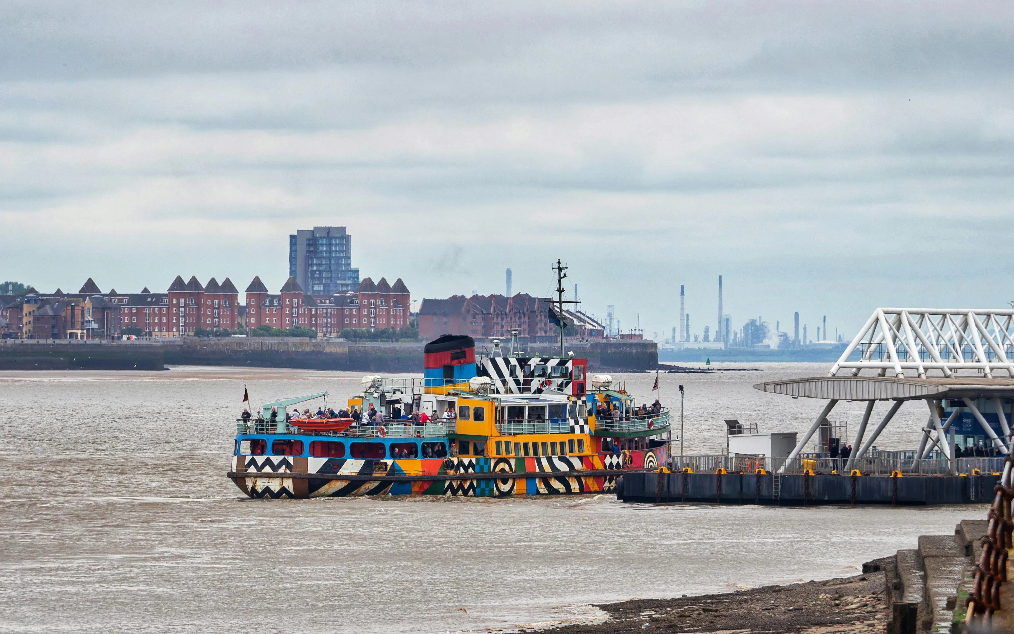 Colorful ferry docked on River Mersey with cityscape in the background.