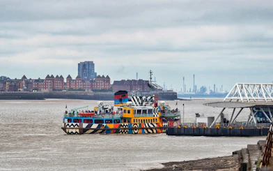 Colorful ferry docked on River Mersey with cityscape in the background.