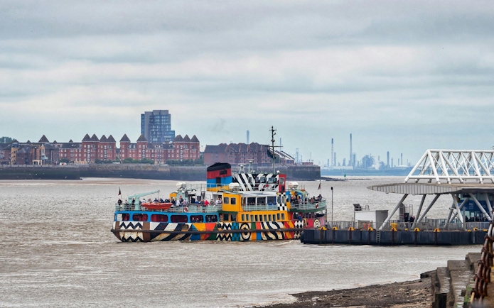Colorful ferry docked on River Mersey with cityscape in the background.