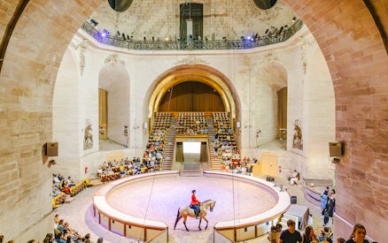 Horse show in the grand arena of the Chateau of Chantilly, France, with an audience watching.