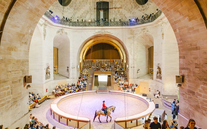 Horse show in the grand arena of the Chateau of Chantilly, France, with an audience watching.
