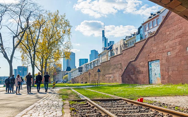 People walking along a path with Frankfurt skyline in the background, part of Skyline Hop-On Hop-Off tour.