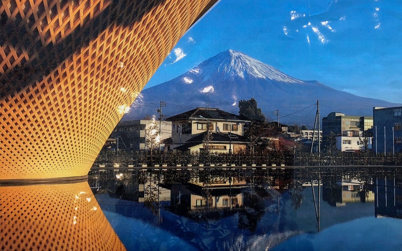 Mt. Fuji with traditional Japanese houses and a modern structure reflected in water.