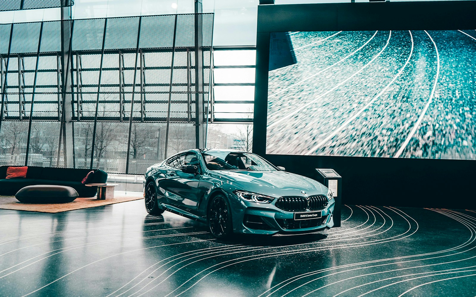 BMW 8 Series Coupe displayed in a modern showroom with large digital screen.