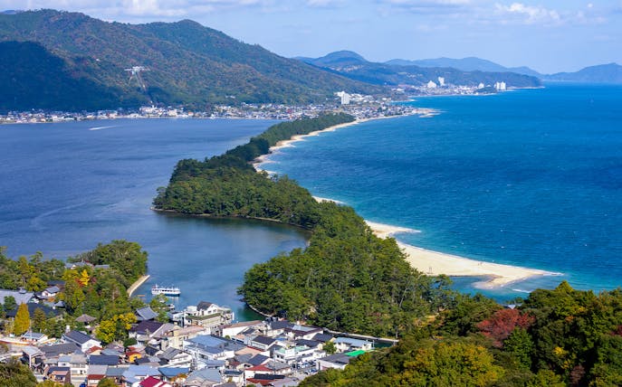 Aerial view of Amanohashidate sandbar in Kyoto, Japan, with surrounding blue waters and lush greenery.