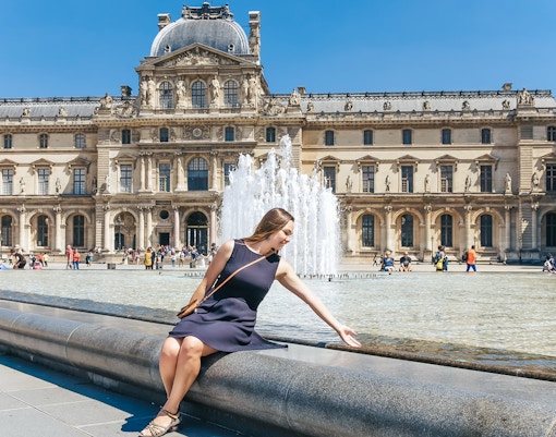 Girl sitting by Louvre Museum fountain, Paris, highlighting a unique day trip viewpoint.