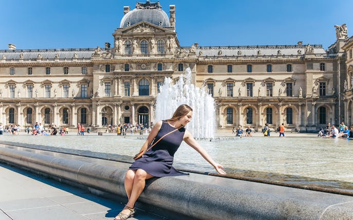 Girl sitting by Louvre Museum fountain in Paris, ideal spot for day trip tour.