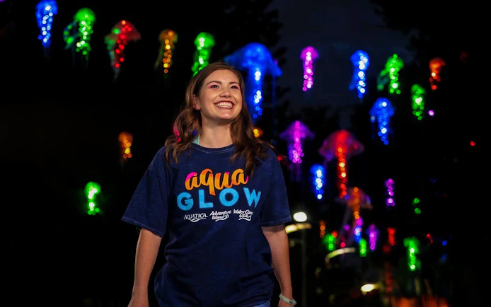 Smiling person at AquaGlow event with colorful jellyfish lights, Aquatica San Antonio.