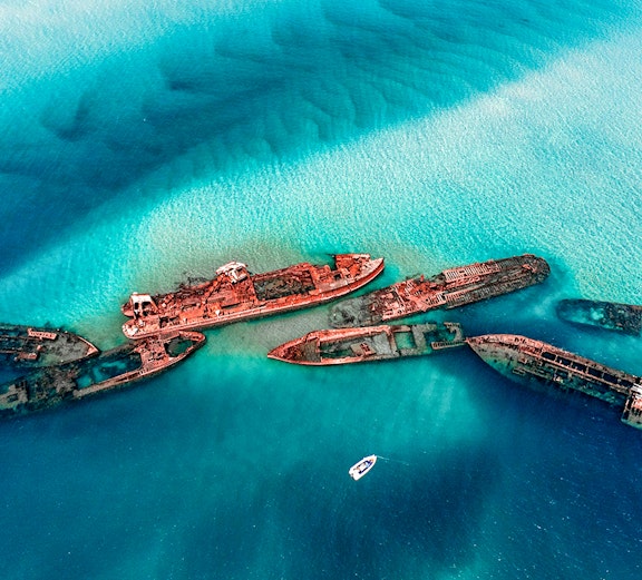 Shipwrecks in turquoise waters near Moreton Island, Australia, with a boat nearby.