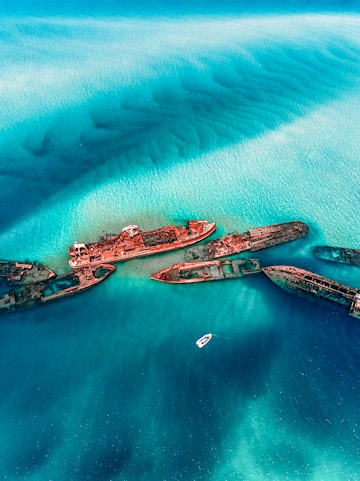 Shipwrecks in turquoise waters near Moreton Island, Australia, with a boat nearby.