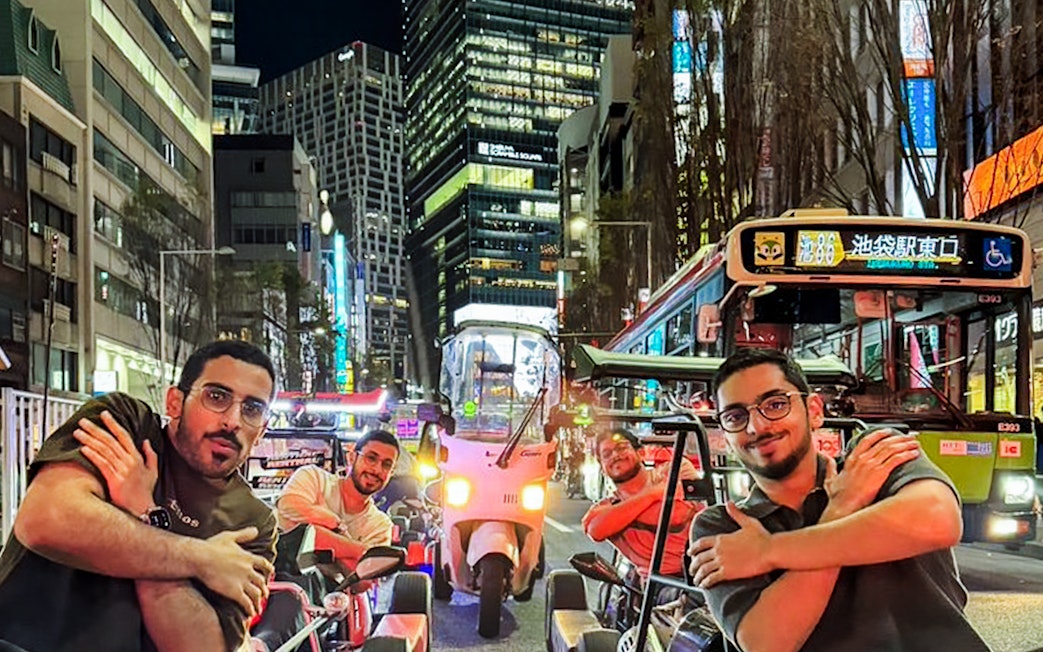 Tourists in go-karts on a busy Tokyo street at night.