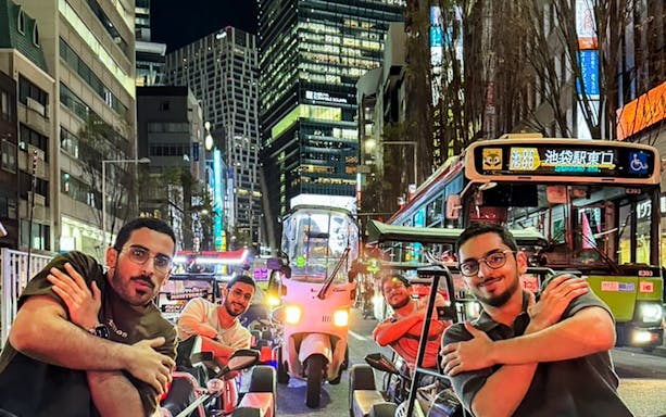 Tourists in go-karts on a busy Tokyo street at night.