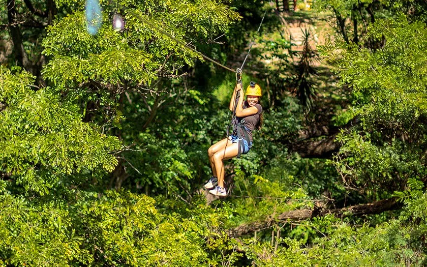 Person ziplining through lush forest with modern braking system.