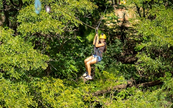 Person ziplining through lush forest with modern braking system.