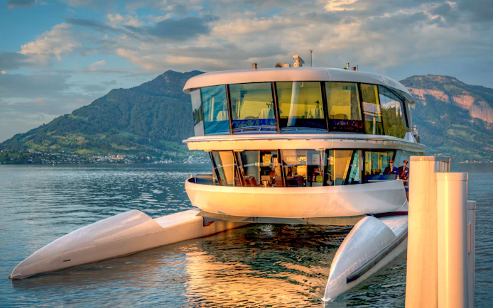 Catamaran docked on a serene lake with mountain backdrop.