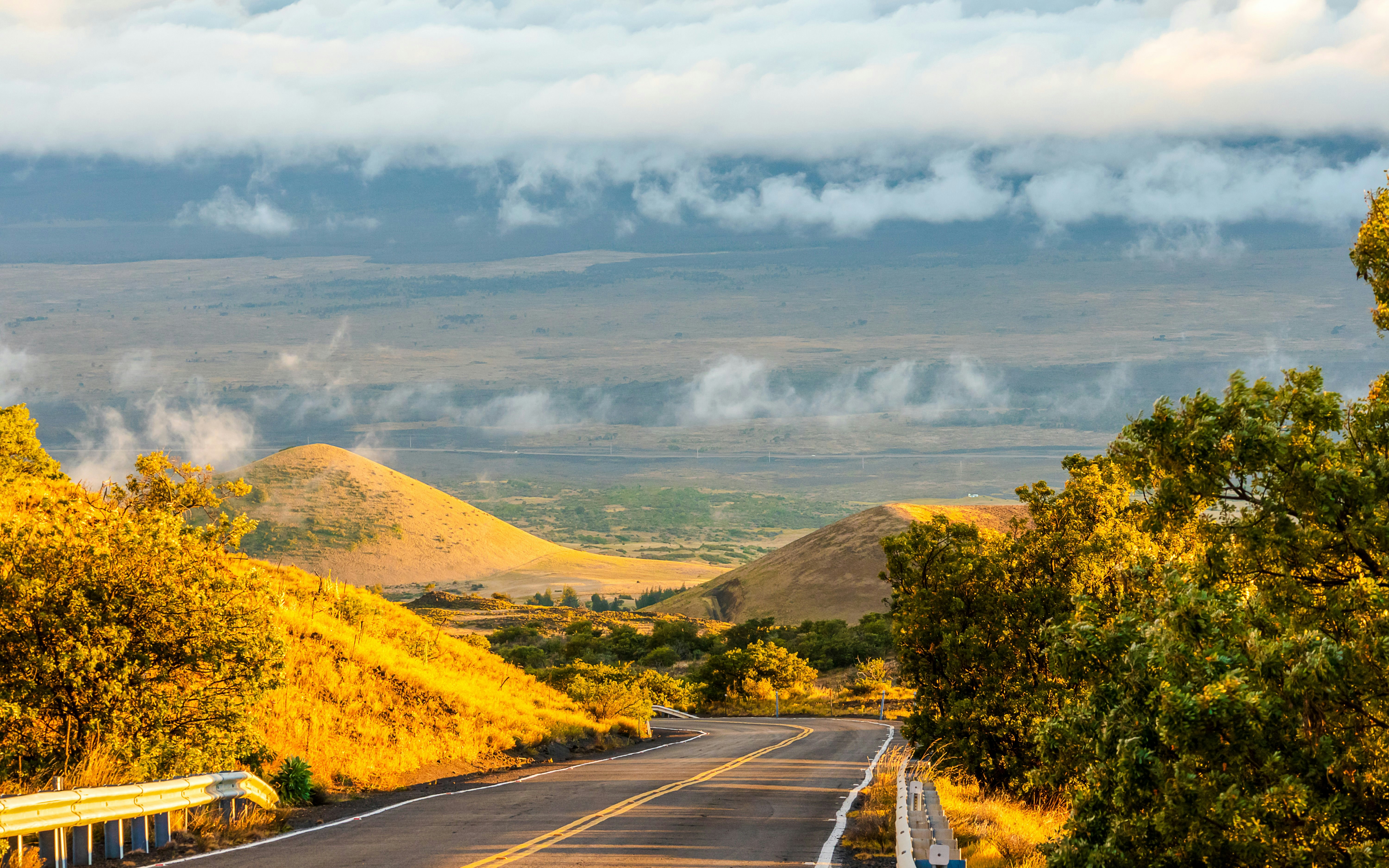 Road leading to Mauna Kea observatories with scenic sunset and rolling hills.